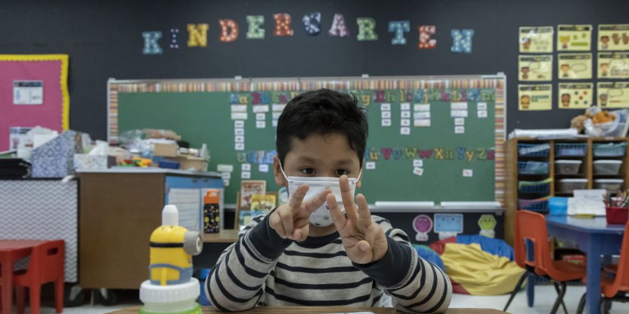 A kindergarten student at a desk works out a math problem on his fingers